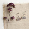 Stamped silver Asmi short loop earrings styled on tan linen with a purple flower