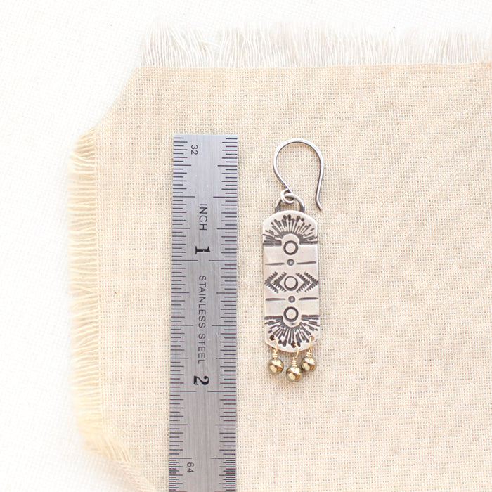 A celestial bar hematite earring next to a ruler for size reference