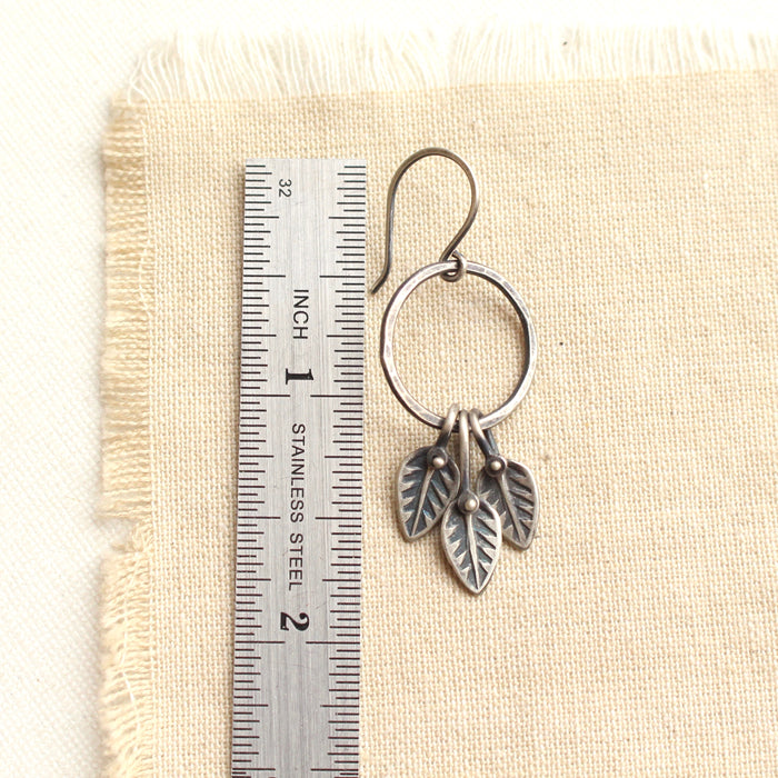 A stamped leaf trio hoop earring next to a ruler for size reference