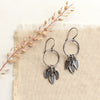 The stamped leaf trio hoop earrings styled on tan linen with dried grass