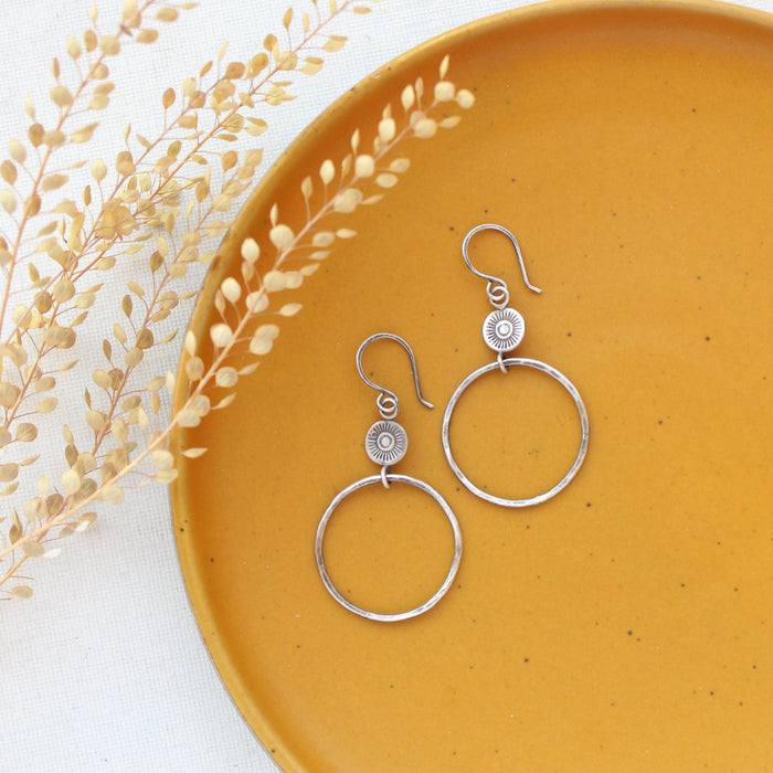 The talara sun hoop earrings styled on a yellow plate with dried grass
