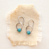 Bright blue apatite spheres hanging delicately off sterling silver bails style on tan linen.