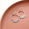Stamped silver Asmi thin blade hoop earrings styled on a red plate