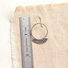 A stamped silver Asmi thin blade hoop earring next to a ruler for size reference