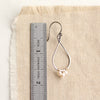 A pearl wrapped teardrop mixed metal hoop earring next to a ruler for size reference