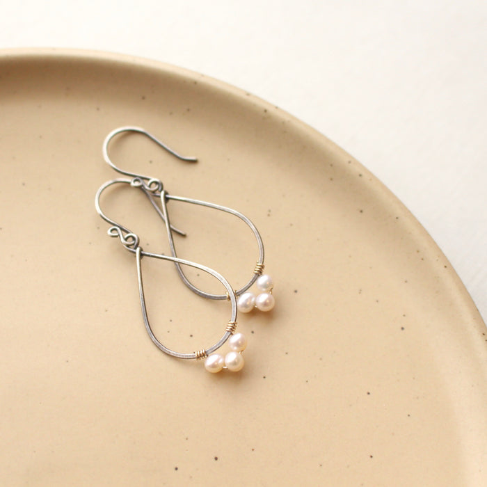 The elegant pearl wrapped teardrop mixed metal hoop earrings styled on a tan plate