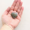 A green and blue labradorite heart stone resting in the palm of a hand