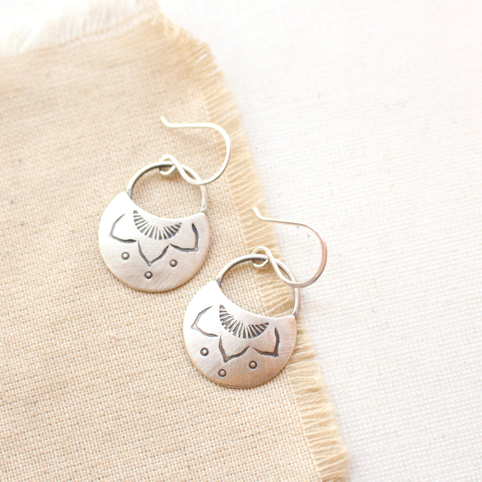 Stamped silver lotus half moon earrings styled on tan linen