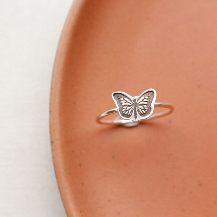 The silver butterfly stacking ring styled on a red plate