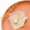 The perfect pearl gold necklace styled on a red plate with linen with dried grass