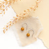 The mookaite lobe hugger earrings styled on tan linen, paper, and dried grass