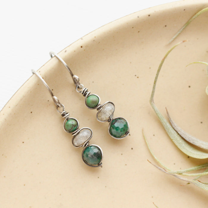 The stacked earthy earrings styled on a tan plate with an air plant