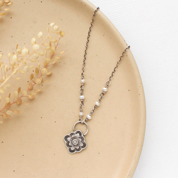 the talara bloom pearl necklace styled on a tan plate with dried grass