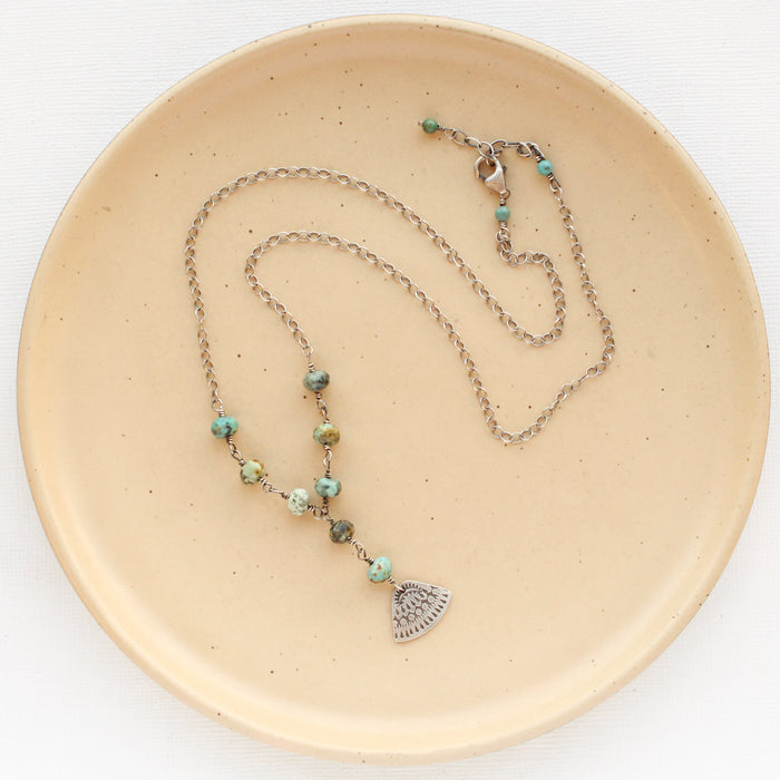 The asmi triangle turquoise lariat necklace styled on a tan plate to show the adjustable lobster clasp closure