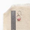A rhodonite la cloche earring next to a ruler for size reference
