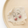 The rhodonite la cloche earrings styled on a tan plate with linen