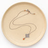 The layered talara sunstone drop necklace styled on a tan plate showing the adjustable lobster clasp closure