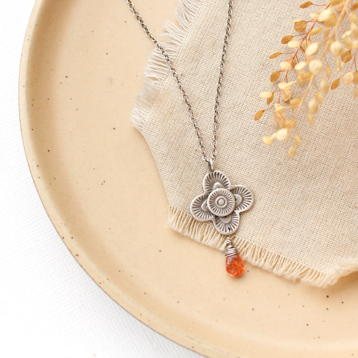 The layered talara sunstone drop necklace styled on a tan plate with linen and dried grass