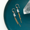 The stacked herkimer diamond gold tassel earrings styled on a blue plate with a crystal