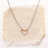 Mixed metal floating heart necklace styled on tan linen