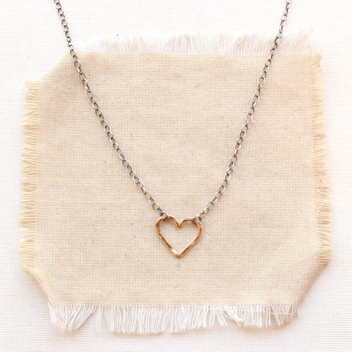 Mixed metal floating heart necklace styled on tan linen