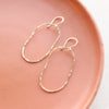 The organic gold hoop earrings styled on an orange plate