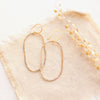 The organic gold hoop earrings styled on tan linen with dried grass