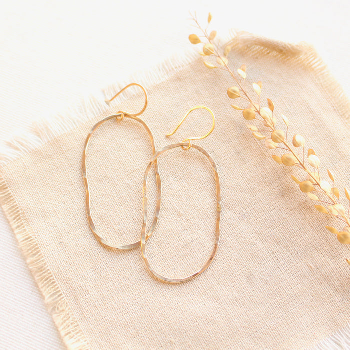 The organic gold hoop earrings styled on tan linen with dried grass