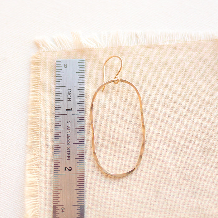 An organic gold hoop earring next to a ruler for size reference