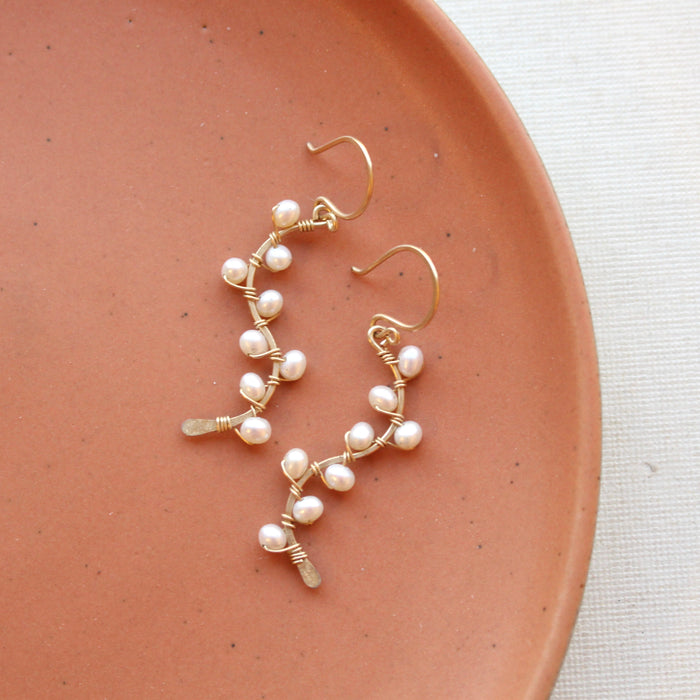 The wrapped pearl gold vine earrings styled on an orange plate