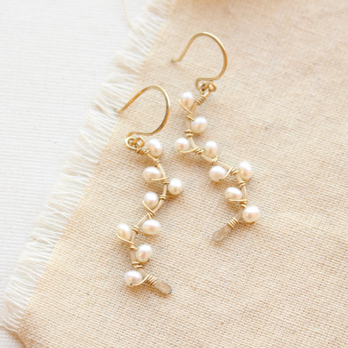 The pearl wrapped gold vine earrings styled on tan linen