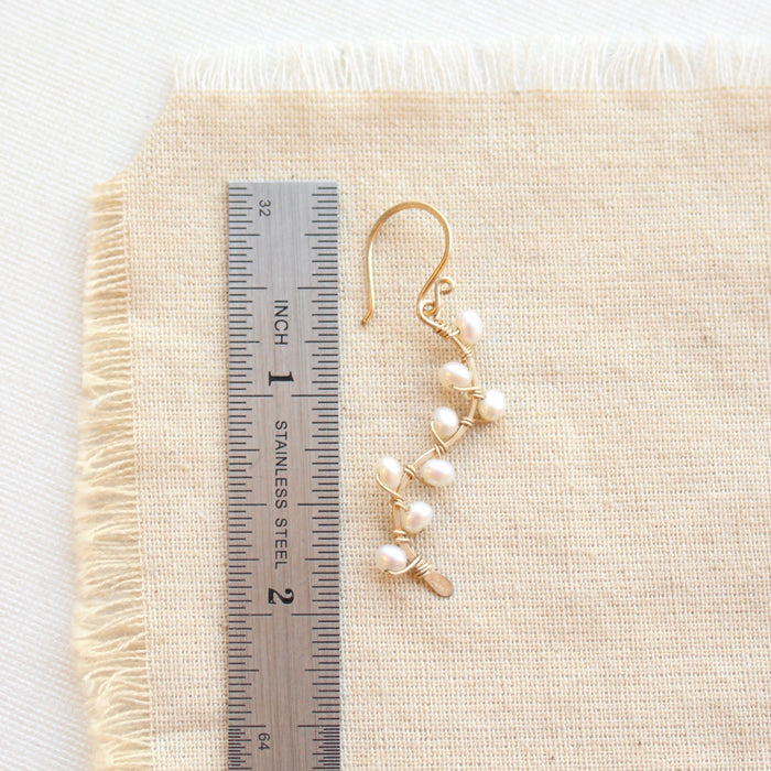 A pearl wrapped gold vine earring next to a ruler for size reference