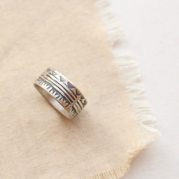 Rustic stamped pattern of triangles and lines, oxidized silver ring styled on tan linen.