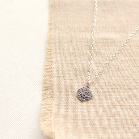 Stamped silver aspen leaf necklace styled on tan linen