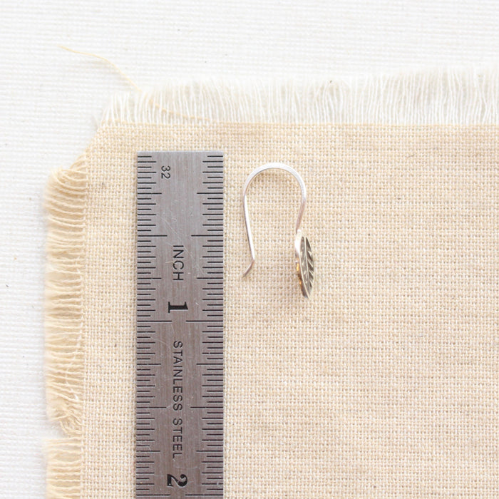 A little leaf lobe hugger earring next to a ruler for size reference