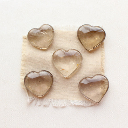 Five smoky quartz heart stones styled on tan linen.