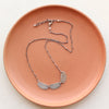 The asmi trio collar necklace styled on a red plate showing the adjustable clasp closure