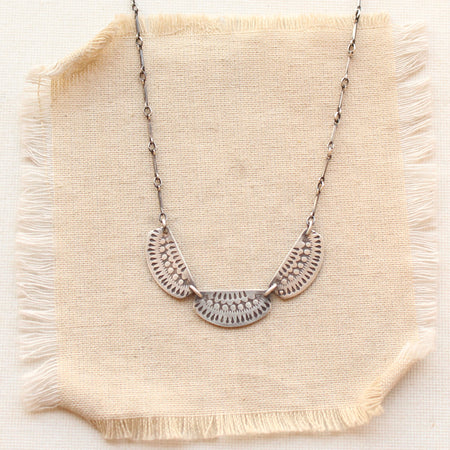 Necklace with hand stamped silver half circles on silver chain styled on tan linen