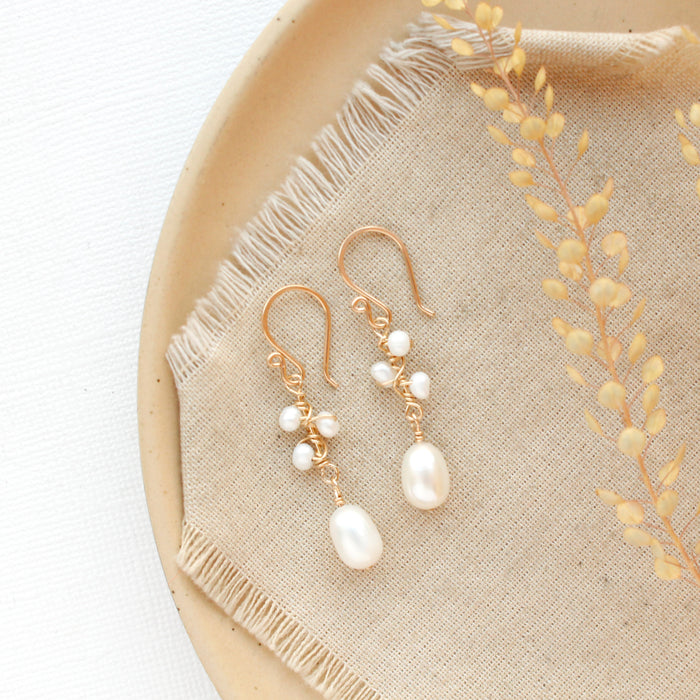 The gold wrapped pearl bud vine earrings styled on a tan plate with linen and dried grass