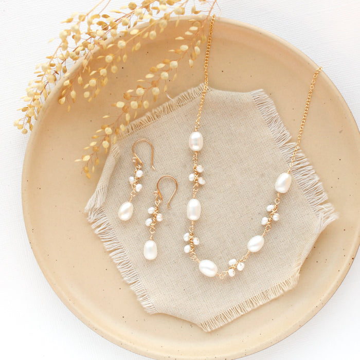 The gold wrapped pearl bud vine earrings styled on a tan plate with the matching necklace
