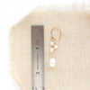 A gold wrapped pearl bud vine earring next to a ruler for size reference
