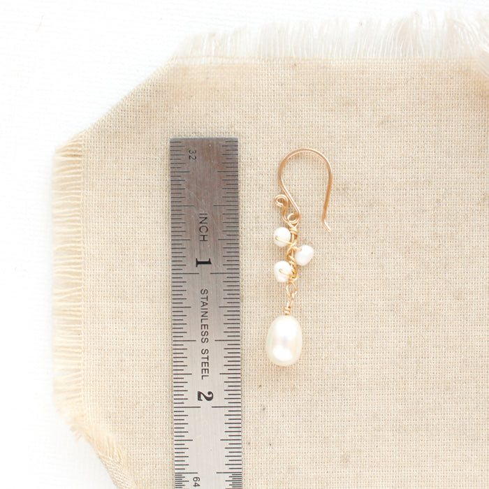 A gold wrapped pearl bud vine earring next to a ruler for size reference