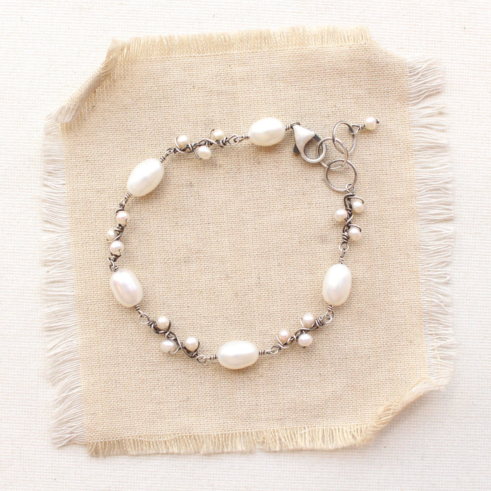 The wrapped pearl bud vine bracelet in silver styled on tan linen