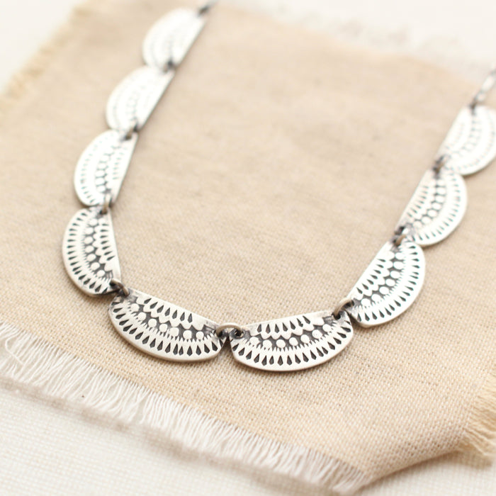 A close up shot of the asmi full collar necklace styled on tan linen