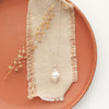 The bright perfect pearl necklace styled on an orange plate with linen and dried grass