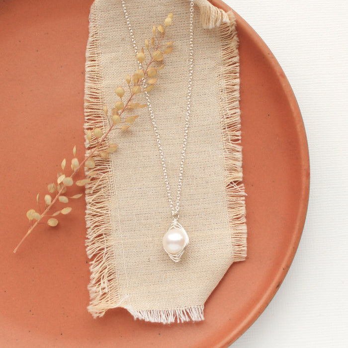 The bright perfect pearl necklace styled on an orange plate with linen and dried grass