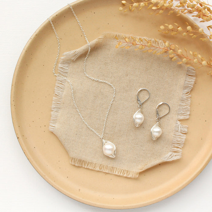 The bright silver perfect pearl necklace styled on a tan plate with the matching earrings