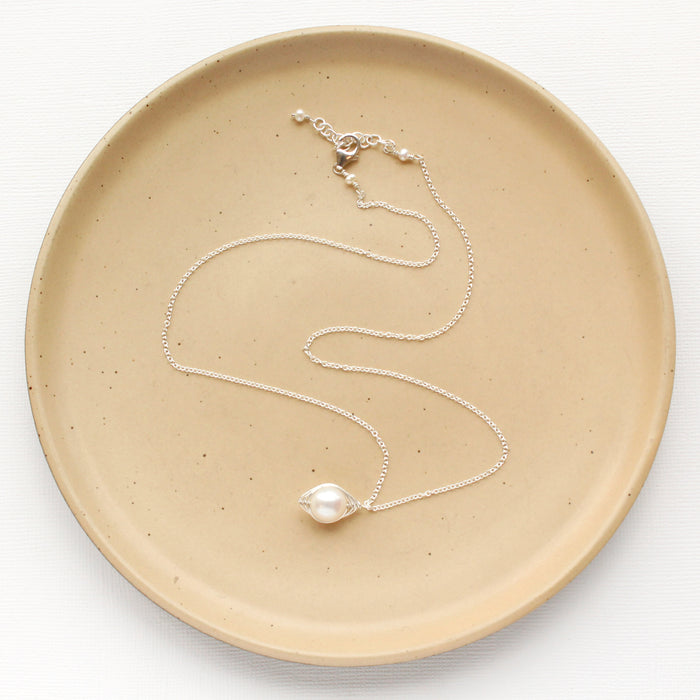 The bright silver perfect pearl necklace styled on a tan plate to show the adjustable lobster clasp closure