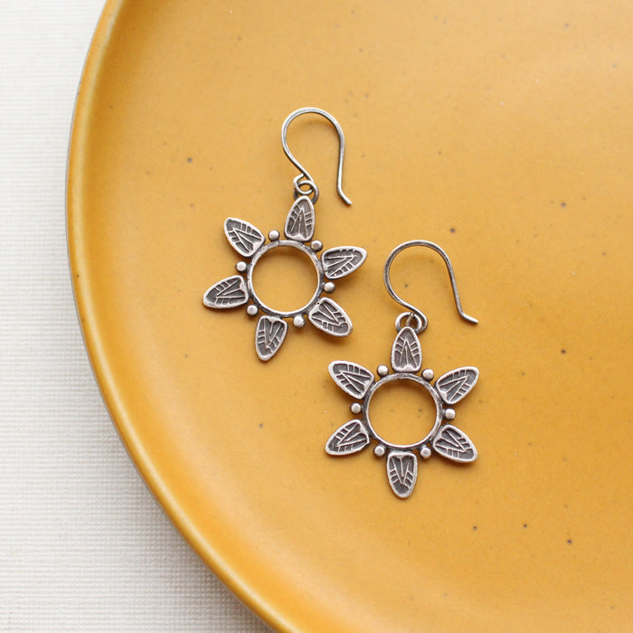The feathered sun earrings styled on a yellow plate
