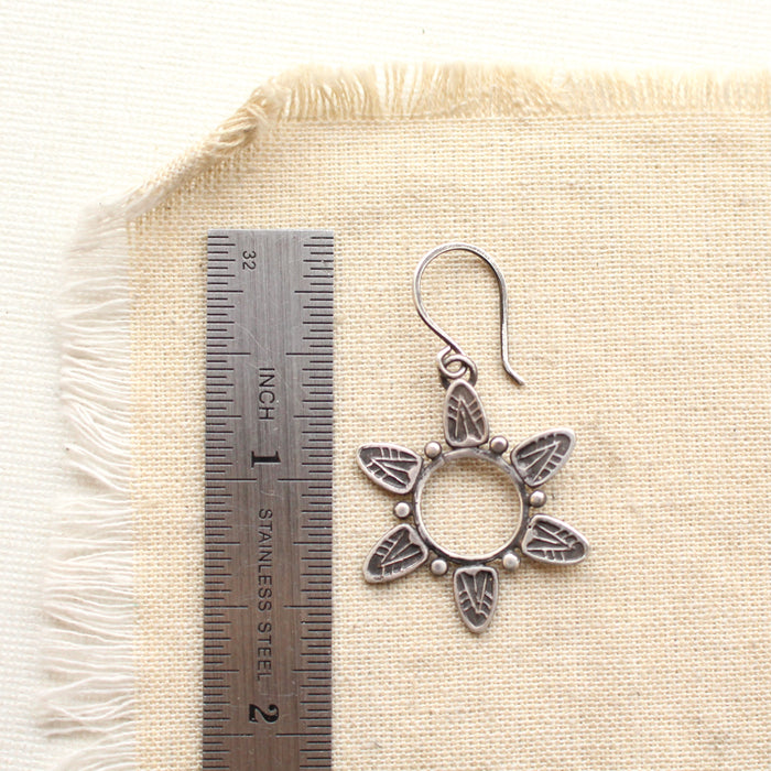 A feathered sun earring next to a ruler for size reference